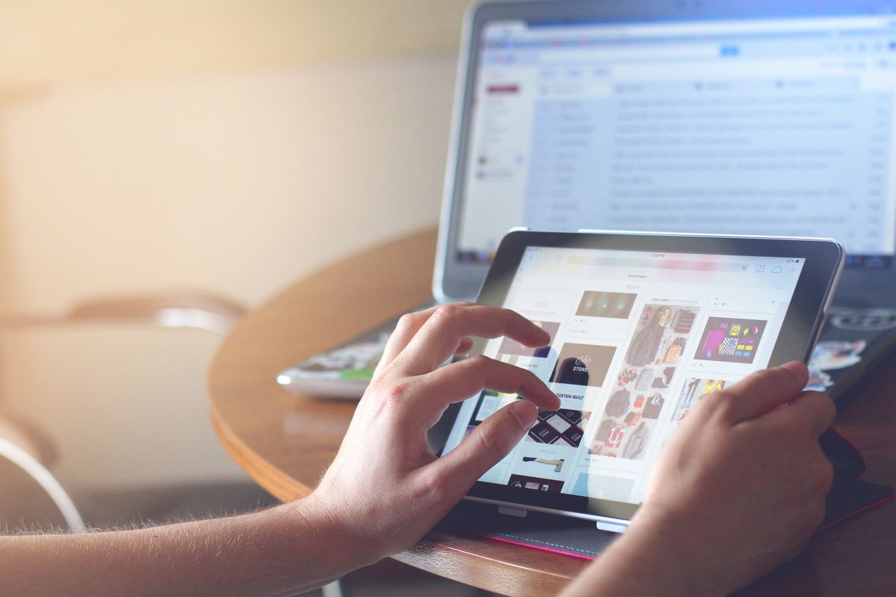 Hands operating a tablet next to a laptop in a home office environment, highlighting online browsing.